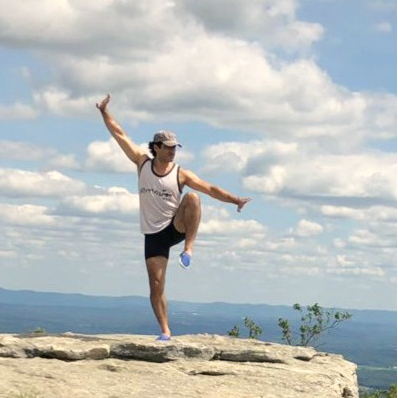 A student balancing on one leg on a rocky overlook.